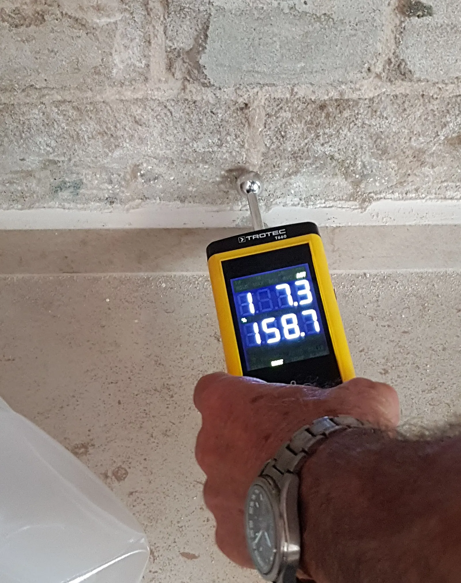 A pin moisture meter held against a masonry wall. Shown on the Attic review page for Huntsville, AL.